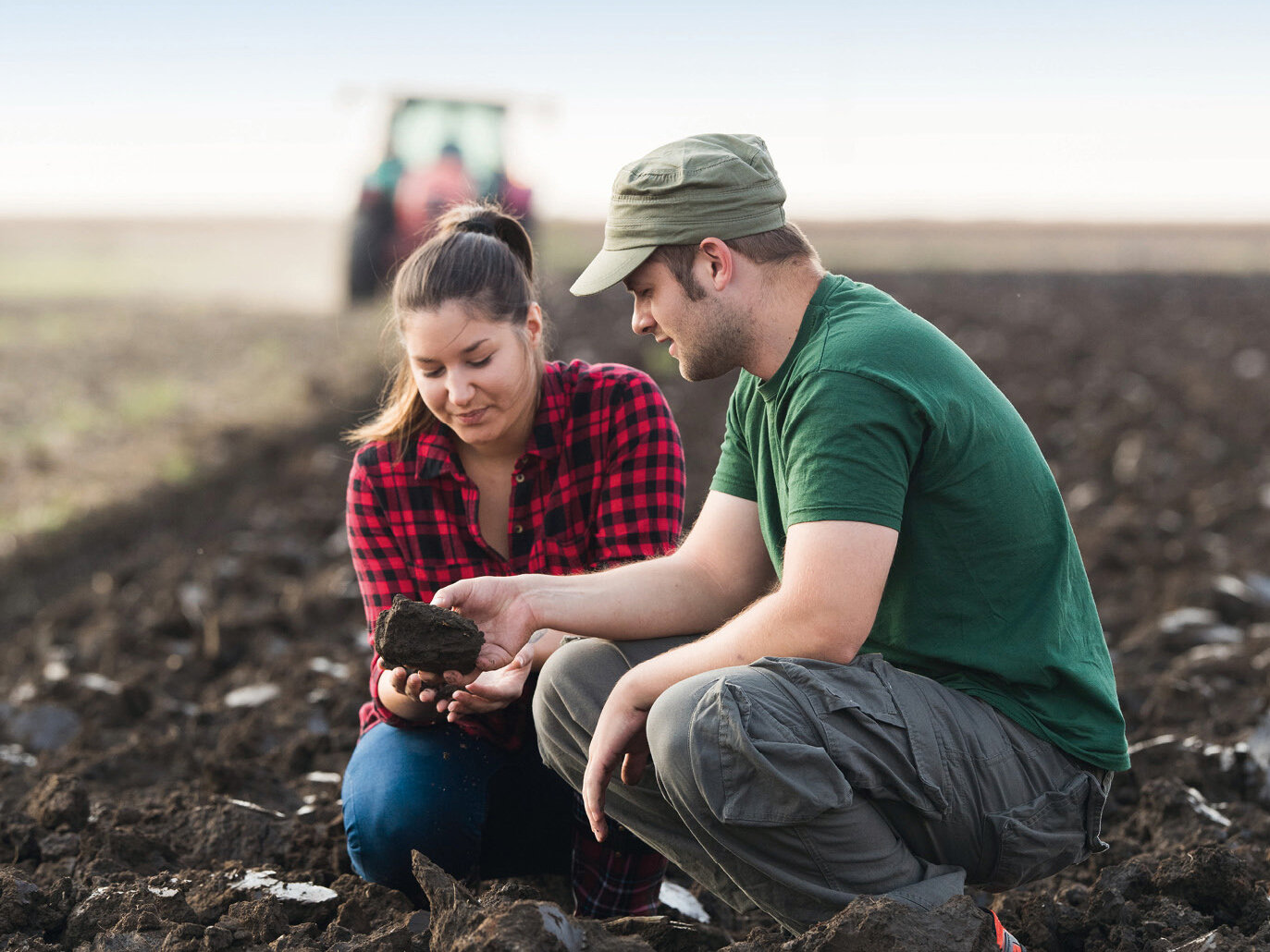 Image of a farming couple kneeling in the field, assessing the soil quality.